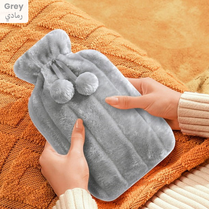 Soft grey hot water bottle with plush cover and pom-pom ties, ideal for soothing aches, warming hands and feet, or use as a cold compress Qatar